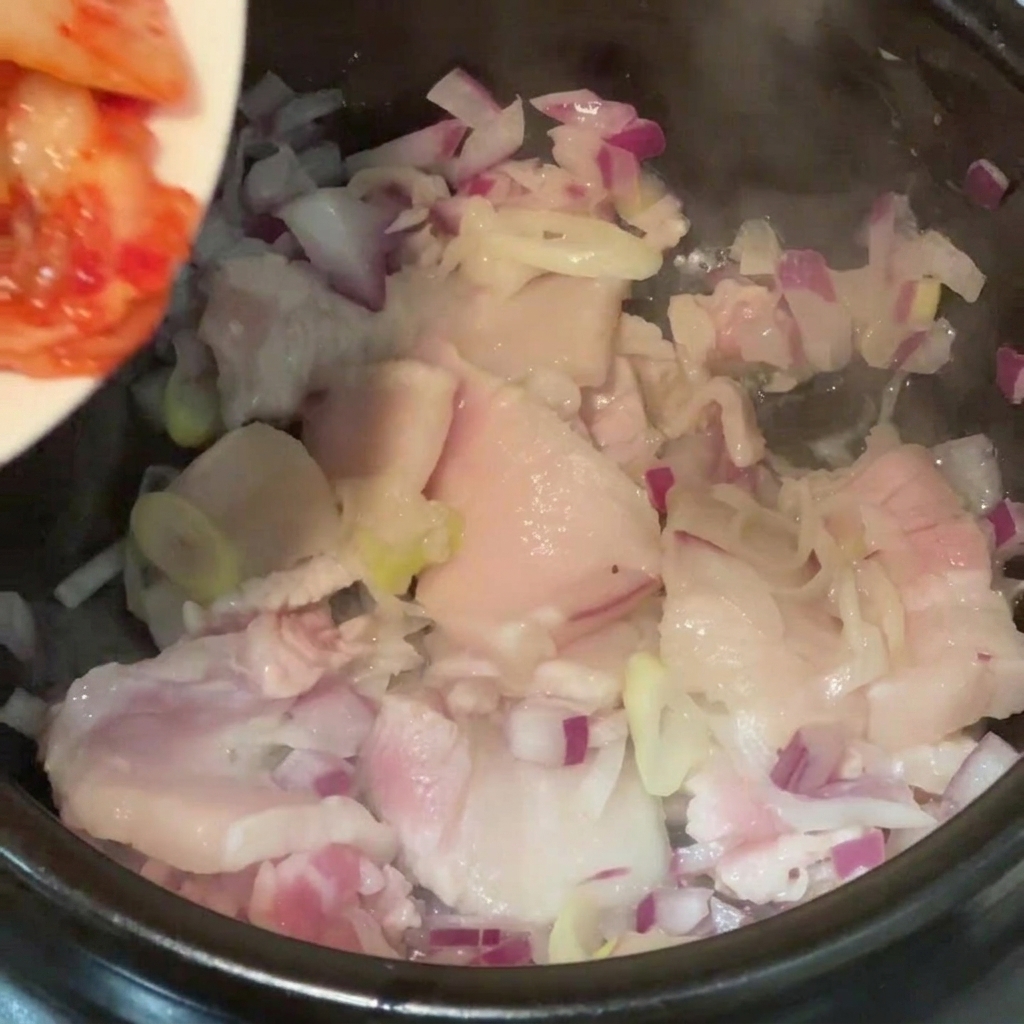 Zsuwanie kwaśnego, posiekanego kimchi z talerza do gorącego garnka z mięsem.