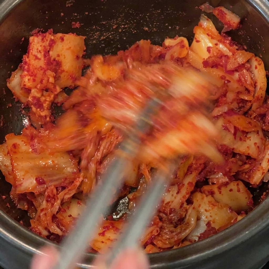 Dokładne mieszanie boczku, kimchi i czerwonych płatków wewnątrz naczynia.