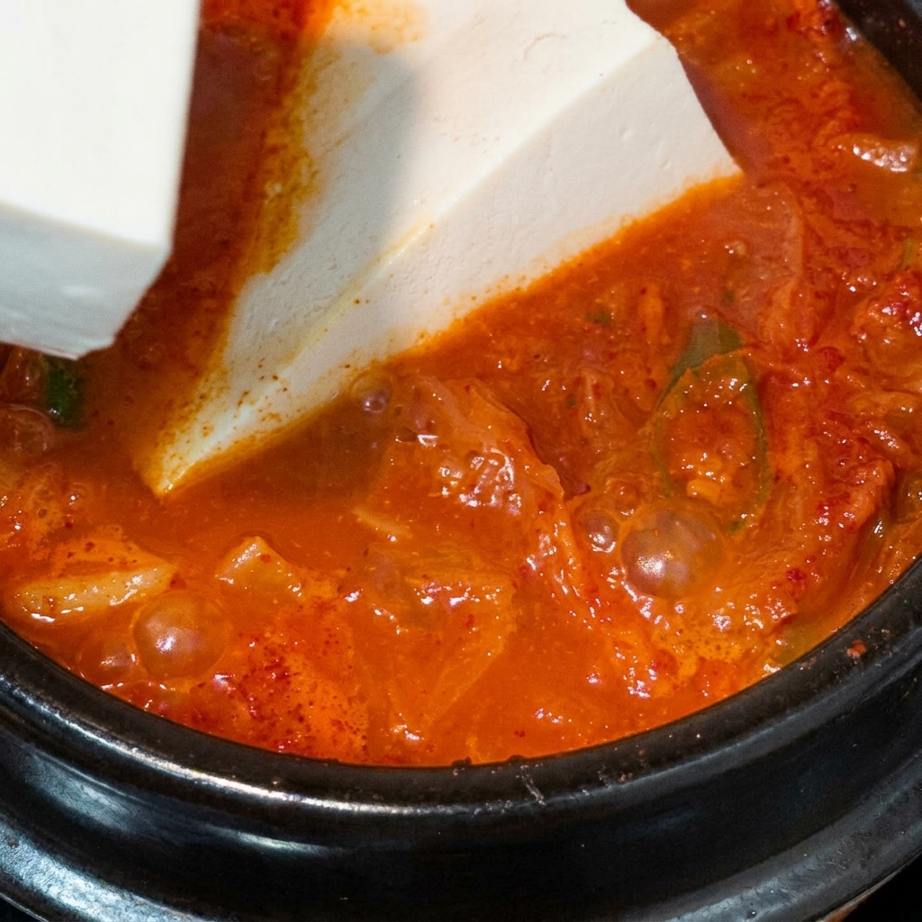 Biała kostka tofu wpuszczana delikatnie na powierzchnię bulgoczącej, wrzącej cieczy.