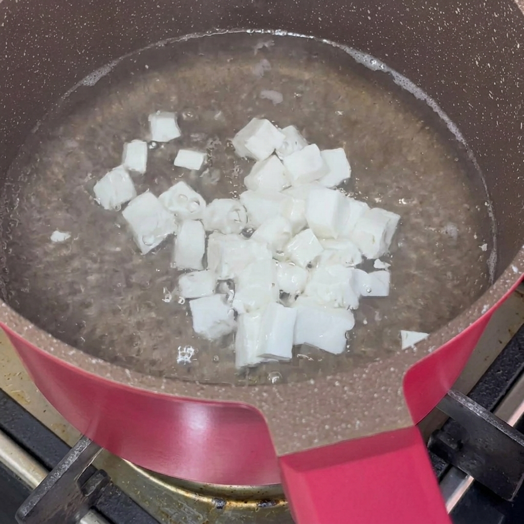 Kawałki tofu blanszowane w garnku z wrzącą wodą.