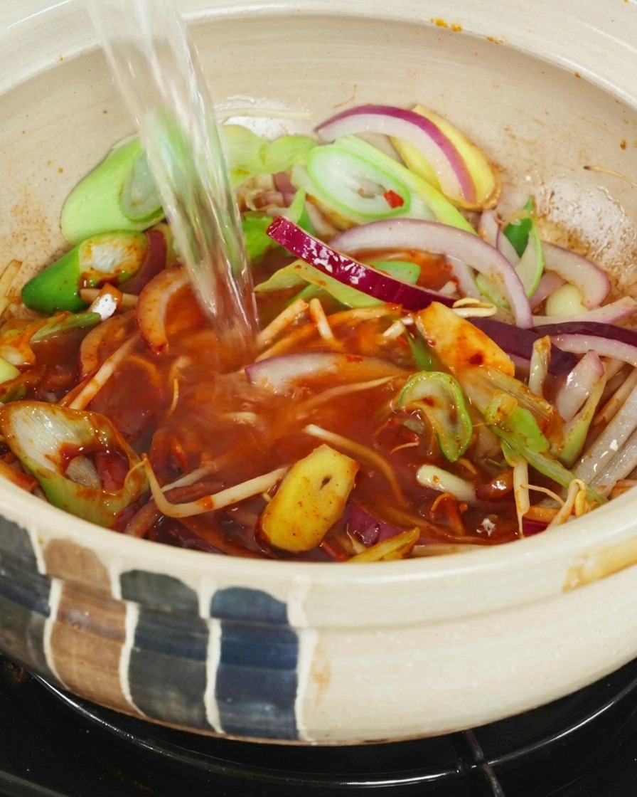 Strumień wrzątku wlewany do garnka z warzywami i pastą chili.