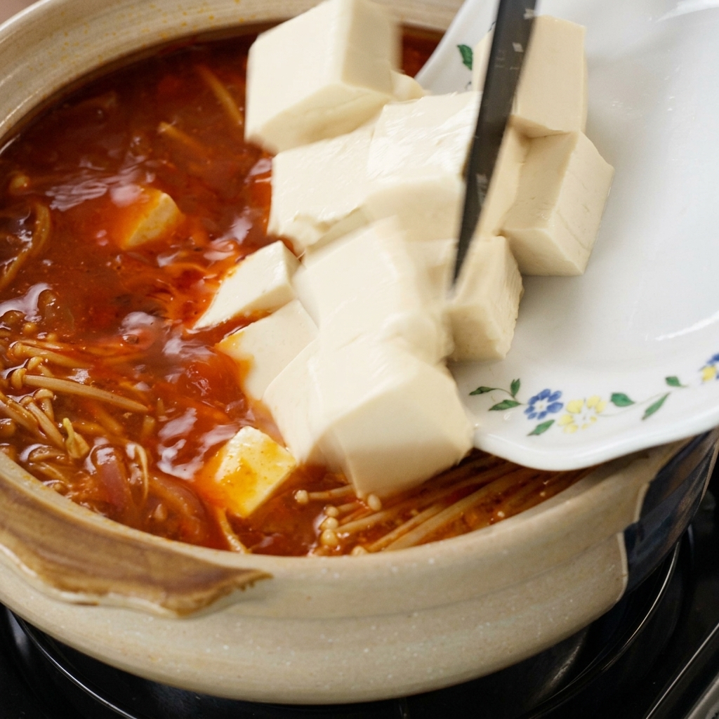 Kostki tofu zsuwane z talerza do garnka z zupą i grzybami enoki.