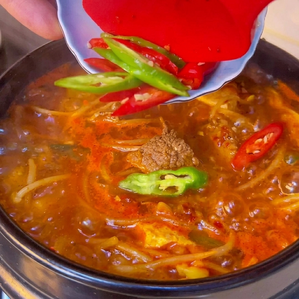 Świeże plasterki zielonego i czerwonego chili zeskrobywane z małej miseczki na powierzchnię gotującej się zupy z tofu.