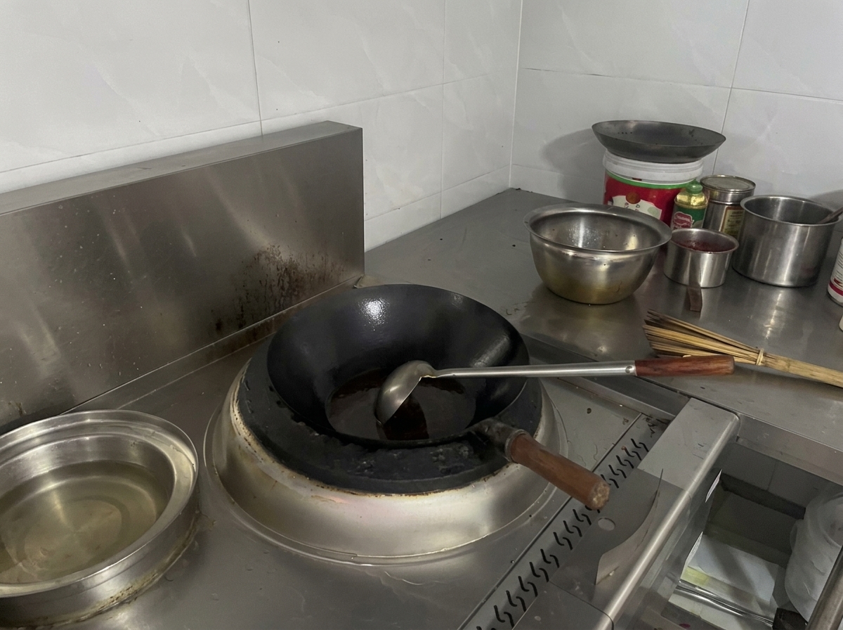 Czarny wok na kuchence wypełniony ciemnobrązowym, gotującym się płynem.