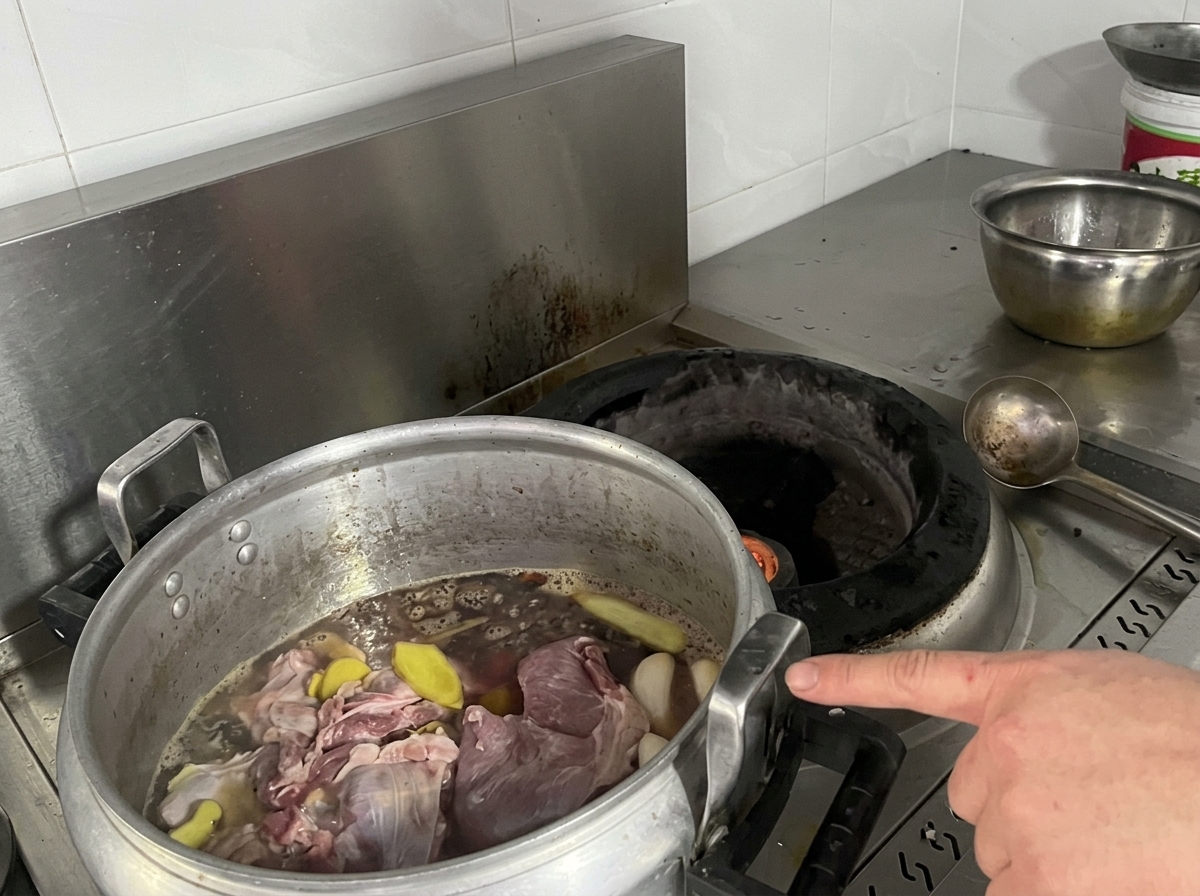 Duży aluminiowy garnek wypełniony surowym mięsem, plastrami imbiru i ciemnym bulionem stojący na kuchence.