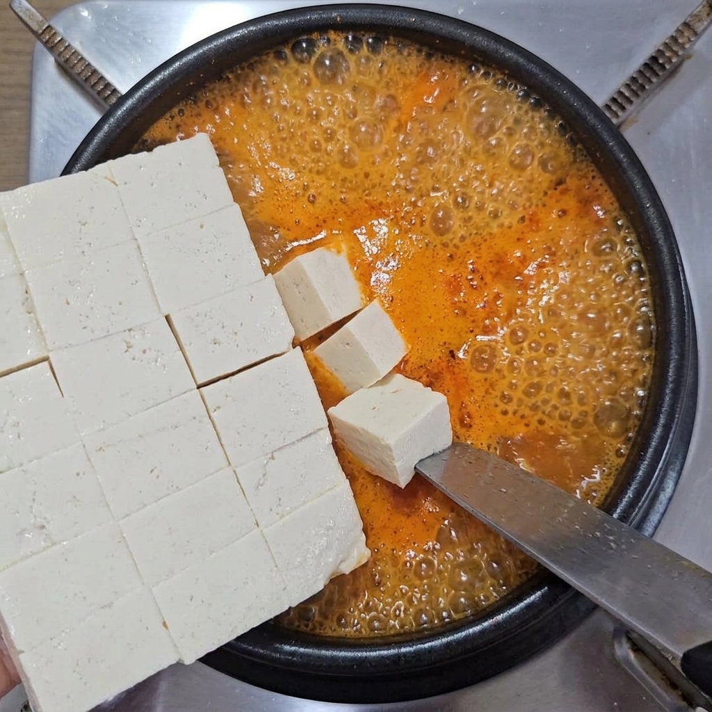 Pokrojone w kostkę miękkie białe tofu delikatnie zsuwane z dużego noża do garnka z bulgoczącą zupą.