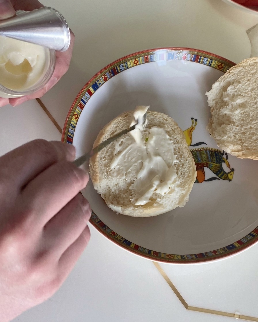 Zbliżenie na łyżkę rozsmarowującą kremowy sos sałatkowy na przekrojonej połówce puszistej bułki.
