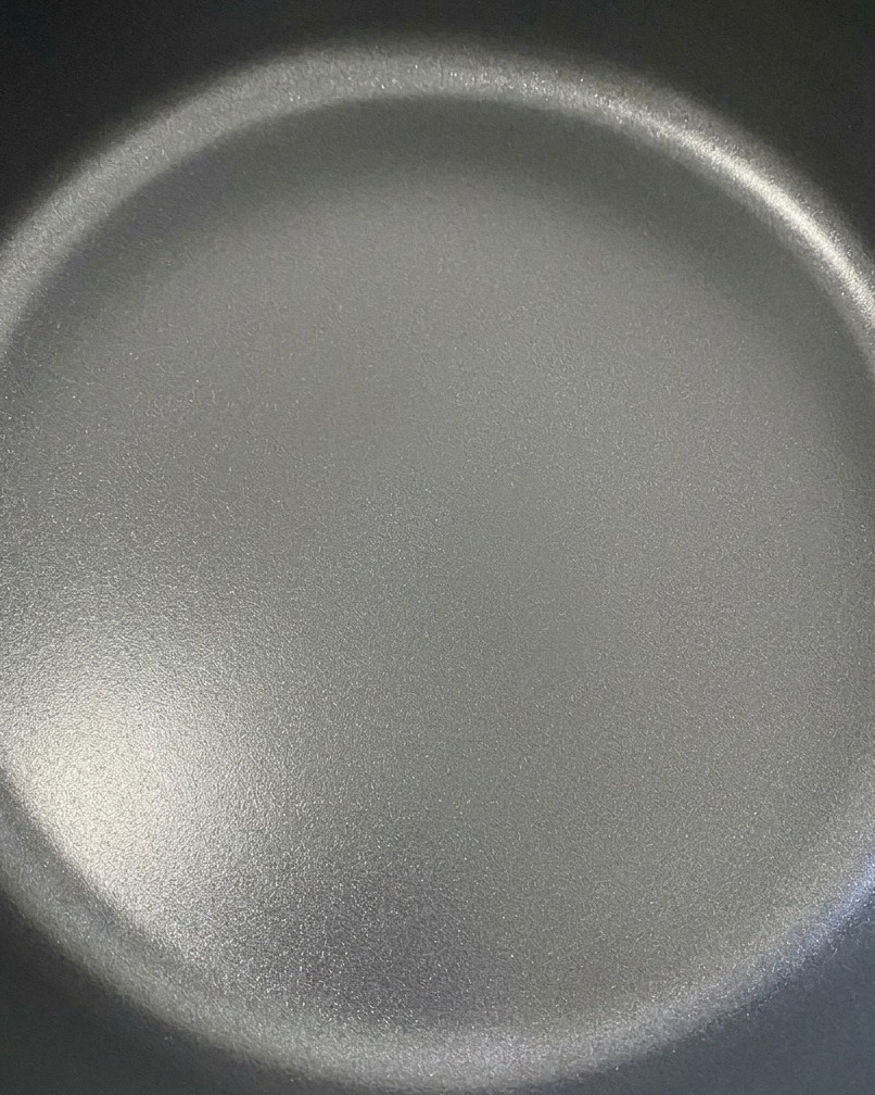 Dwa plastry sera cheddar topiące się na doprawionych kotletach wołowych na ciemnej patelni.