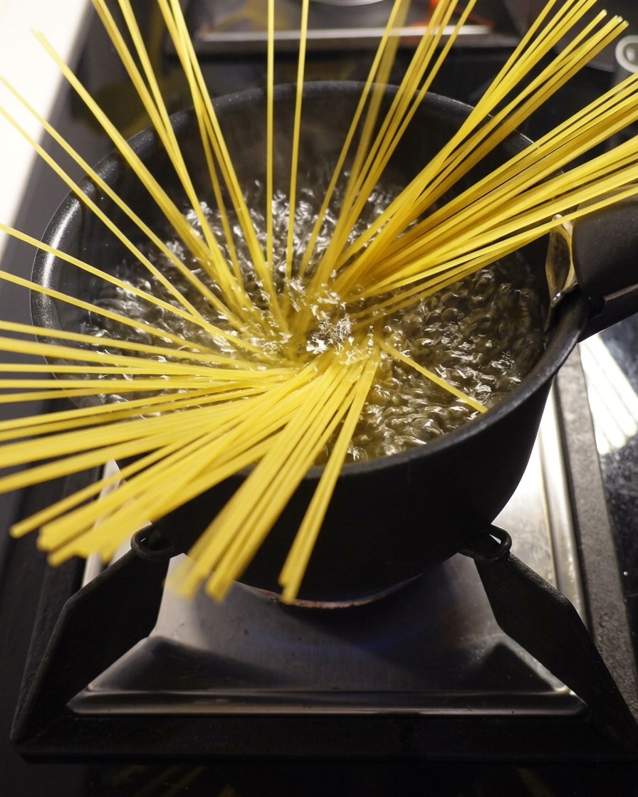 Suchy makaron spaghetti wkładany do dużego garnka z gotującą się wodą.