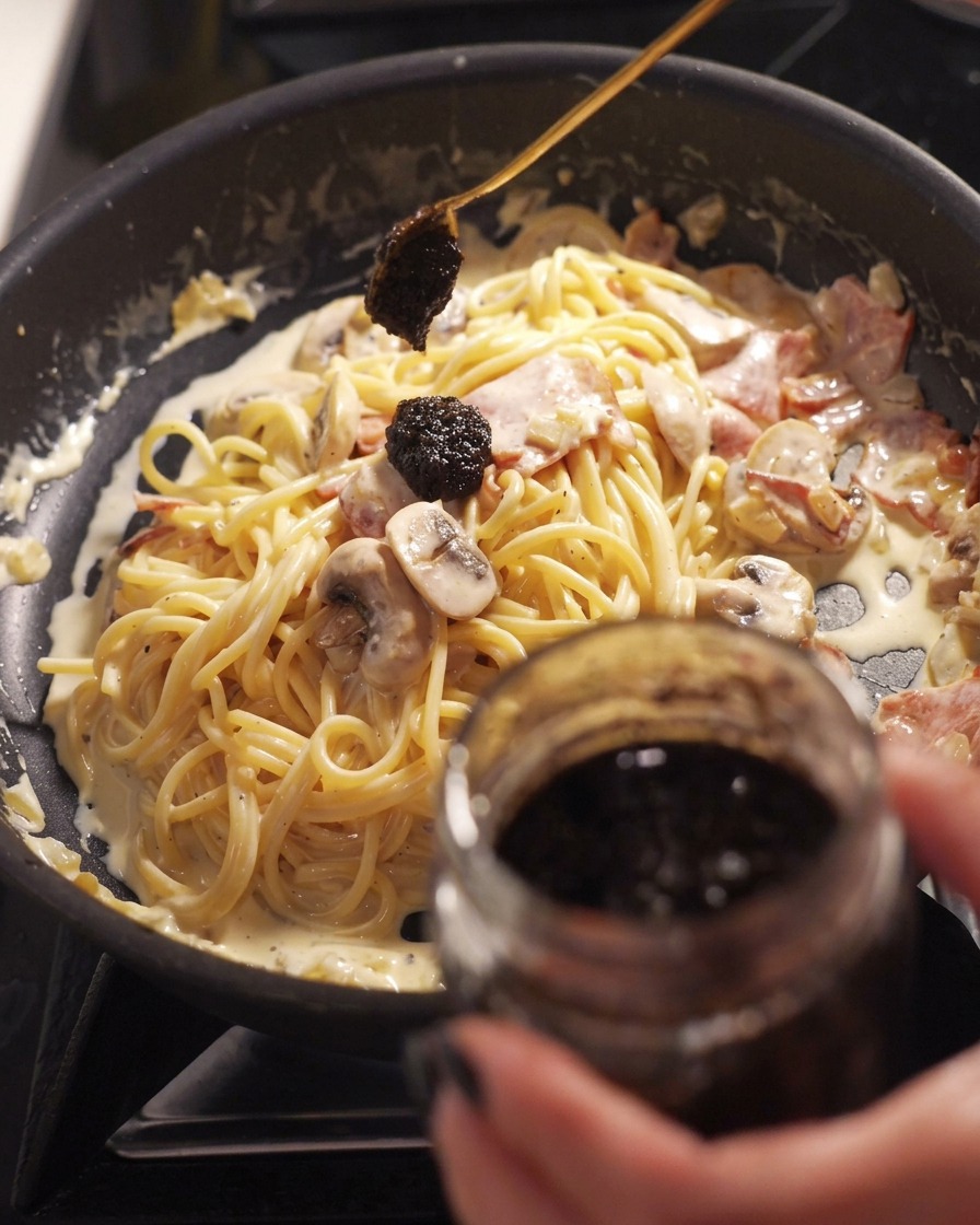 Łyżka ciemnej pasty z czarnej trufli dodawana na patelnię ze śmietanowym spaghetti, boczkiem i pieczarkami.