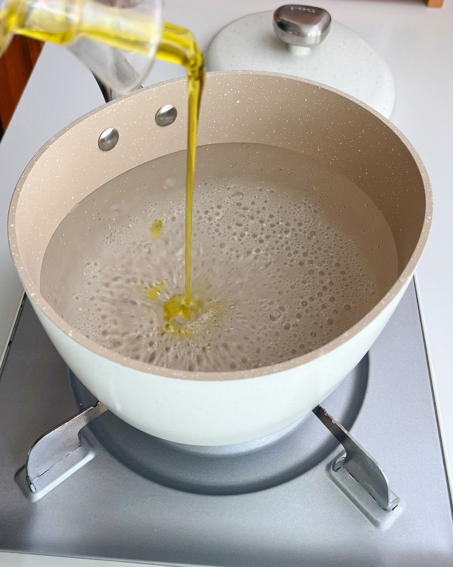 Nitki spaghetti gotujące się w garnku z wodą i oliwą.