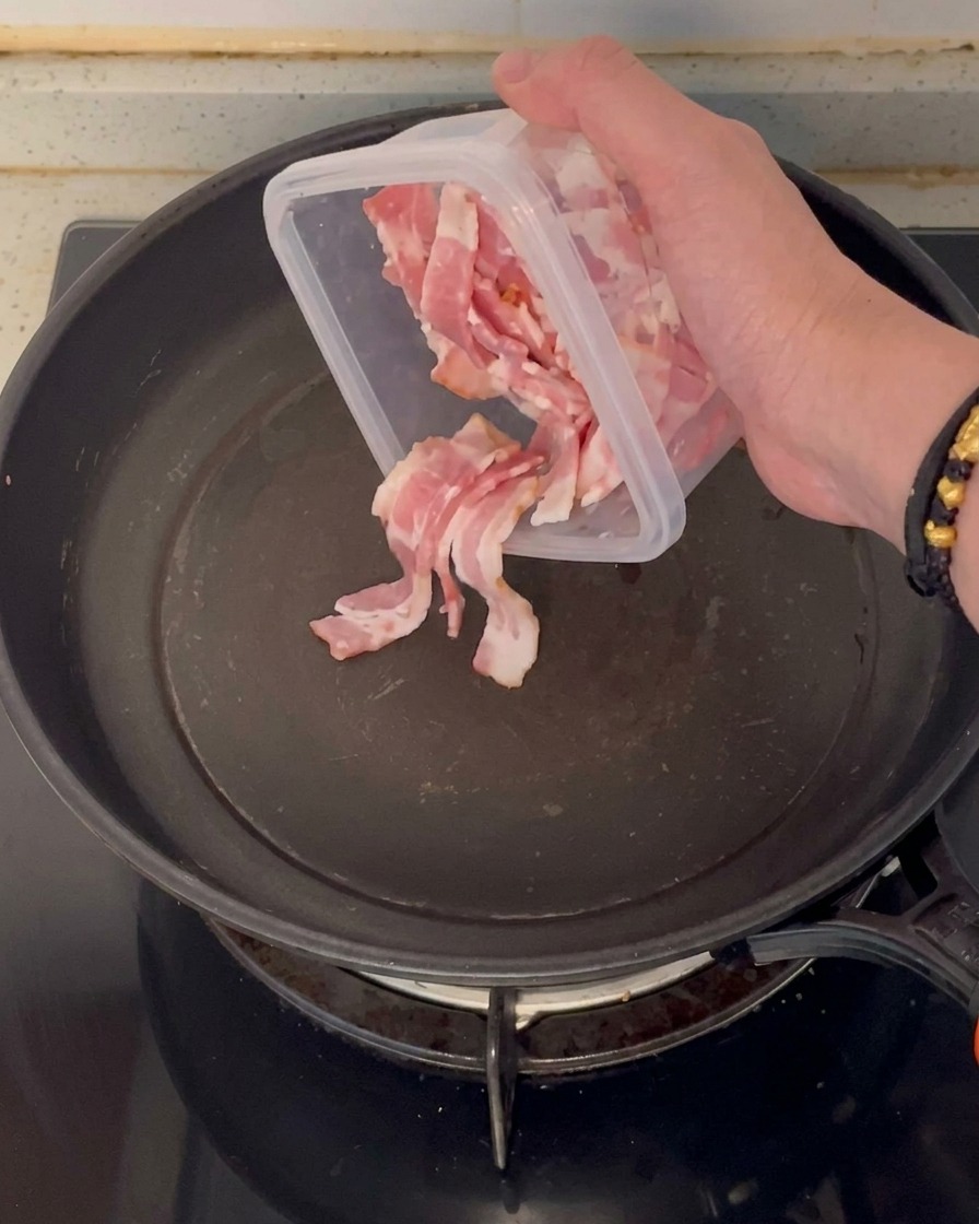 Posiekane kawałki surowego boczku dodawane do czystej, zimnej patelni nieprzywierającej.