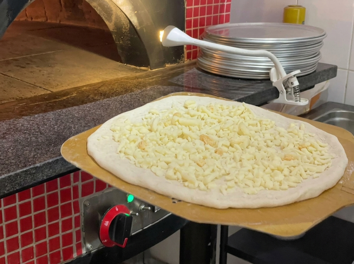 Pizza jest przenoszona do nagrzanego pieca kamiennego za pomocą drewnianej łopaty.