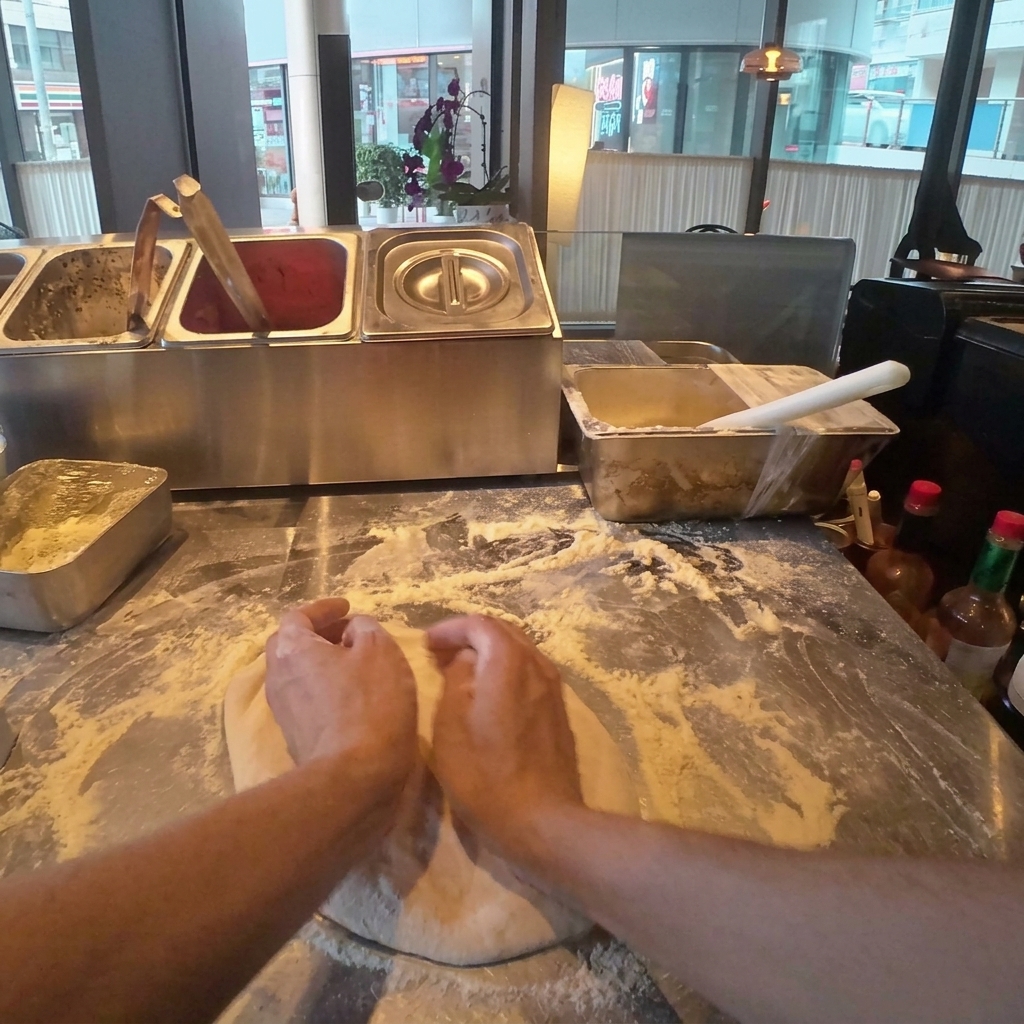 Ciasto na pizzę delikatnie dociskane i rozciągane do okrągłego kształtu na oprószonej mąką drewnianej powierzchni.