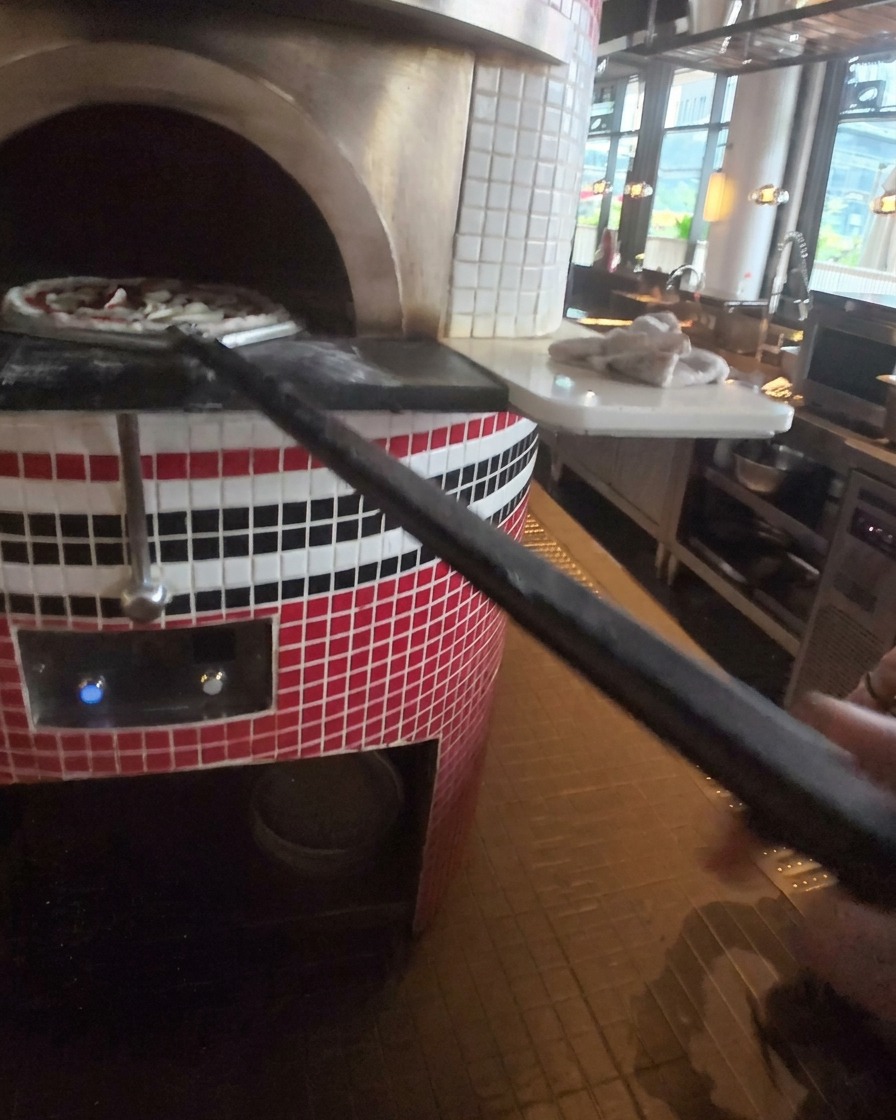 Pizza wsuwana do gorącego pieca kamiennego za pomocą metalowej łopaty na długiej rączce.