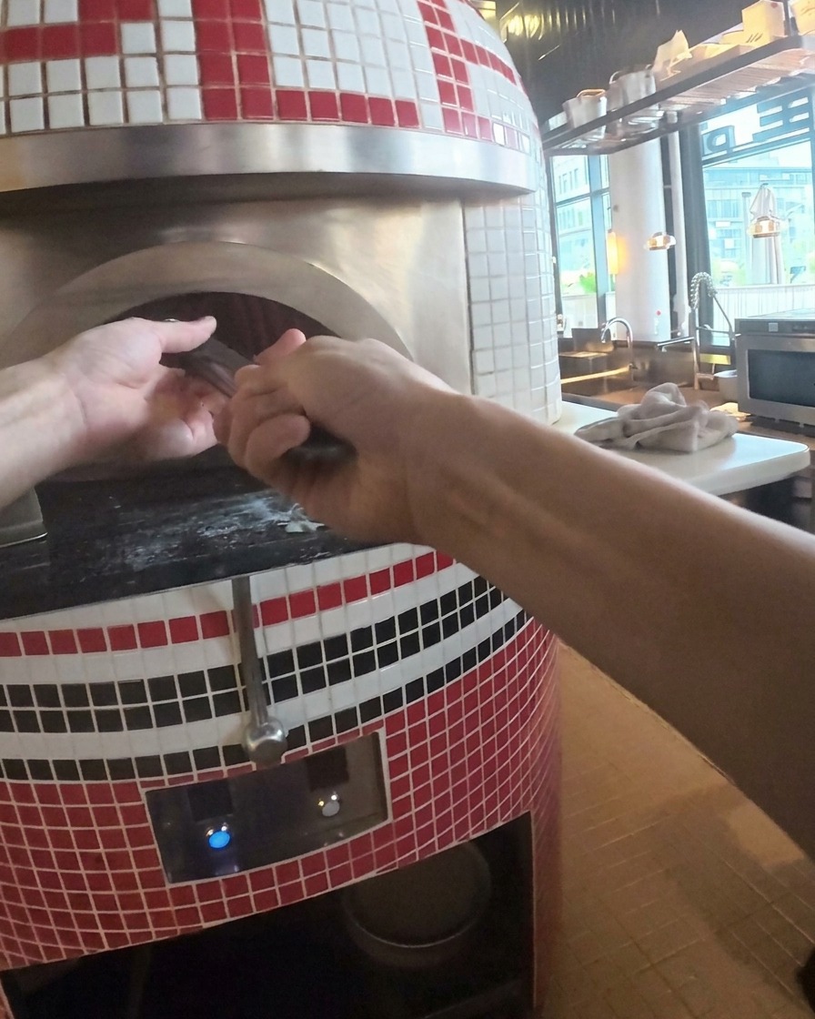 Gorąca, upieczona pizza wyjmowana z pieca kamiennego za pomocą metalowej łopaty.
