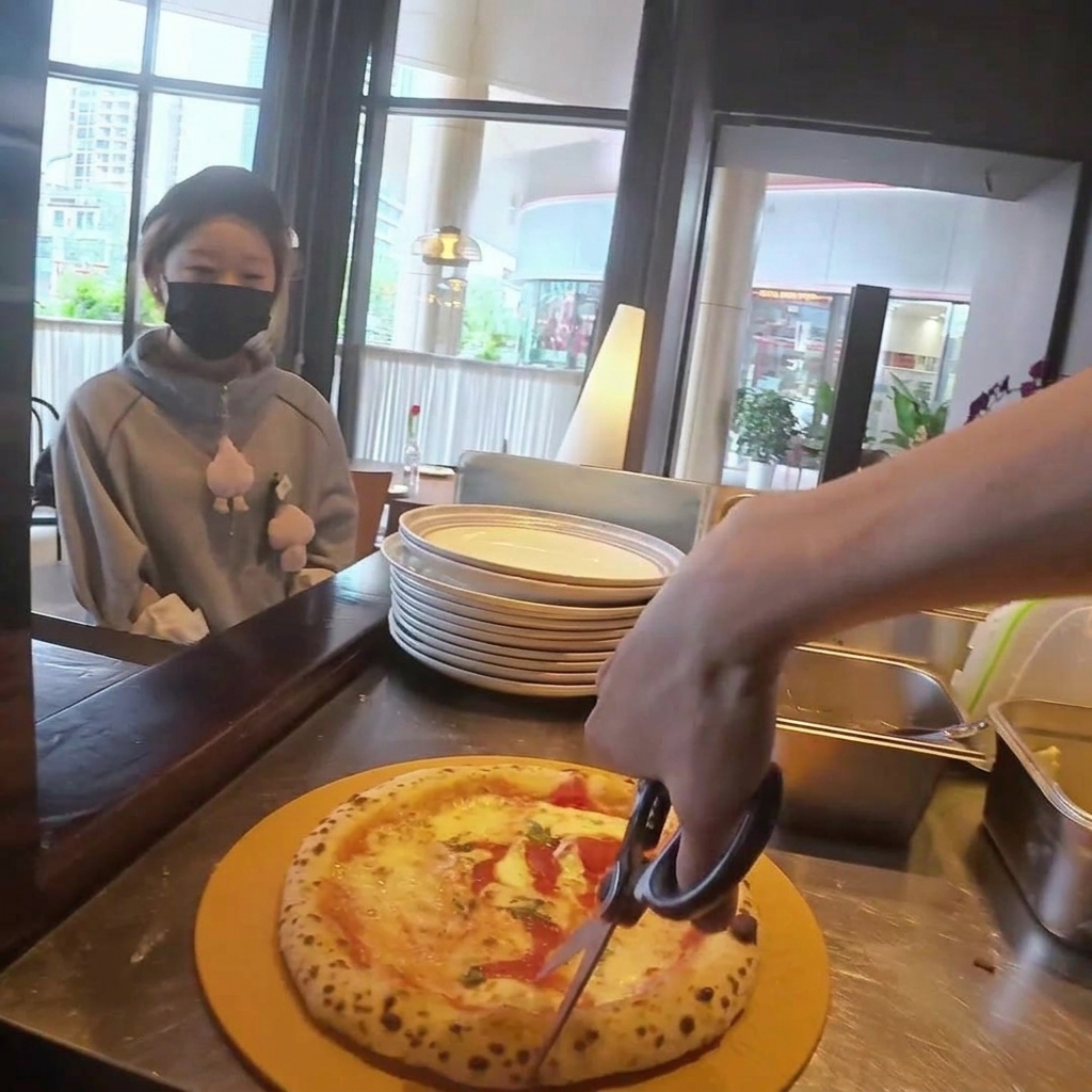Pizza krojona w trójkąty za pomocą okrągłego noża do pizzy na drewnianej desce.
