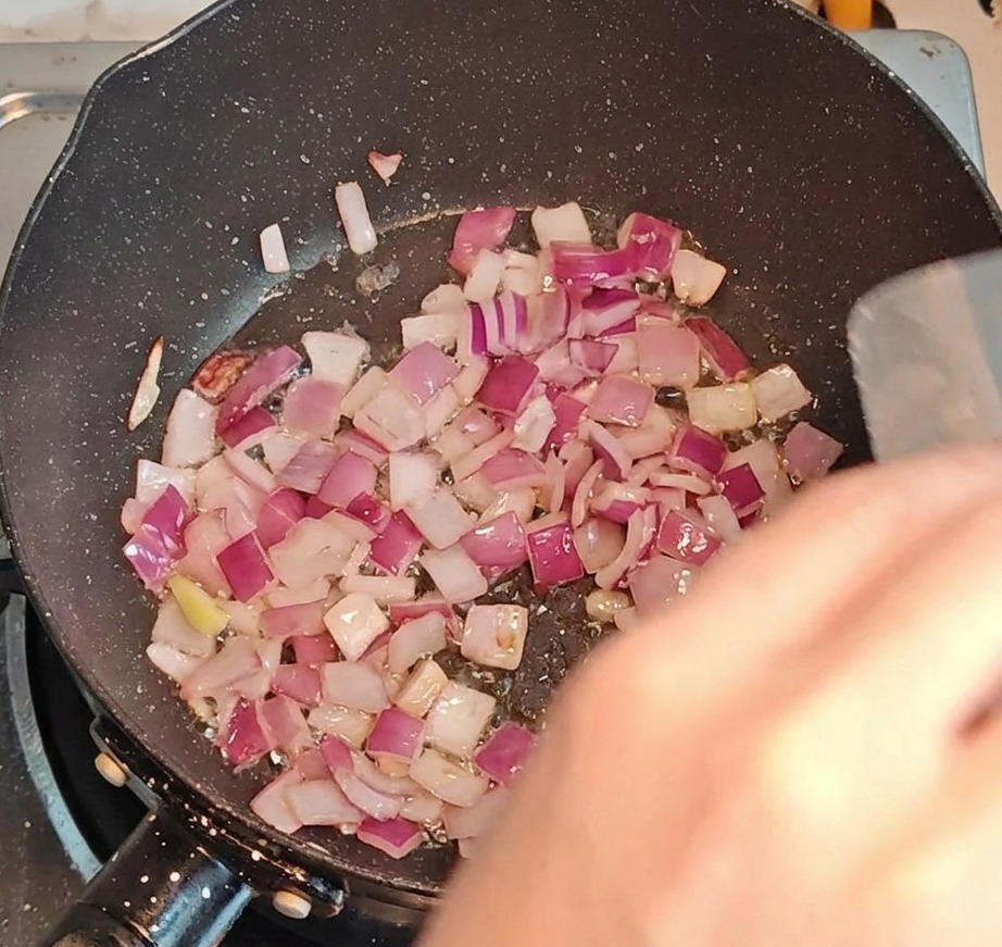 Kawałki boczku z cebulą smażące się na gorącej patelni.