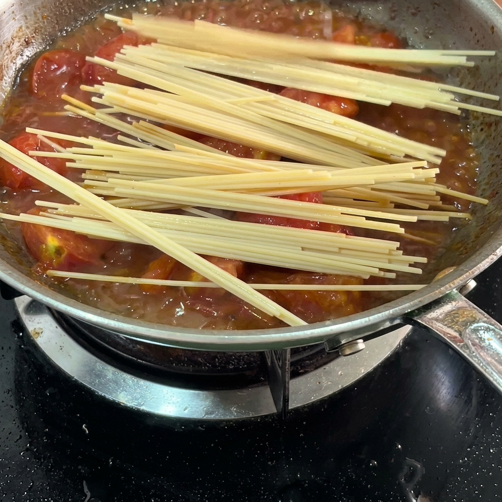 Długie nitki spaghetti zanurzające się w sosie pomidorowym na patelni.