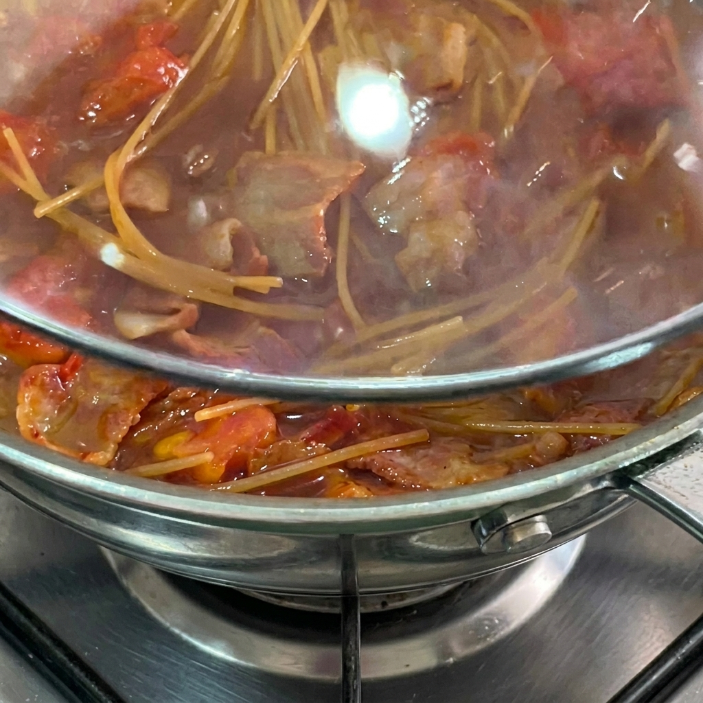Spaghetti duszące się w sosie pomidorowym pod szklaną pokrywką.
