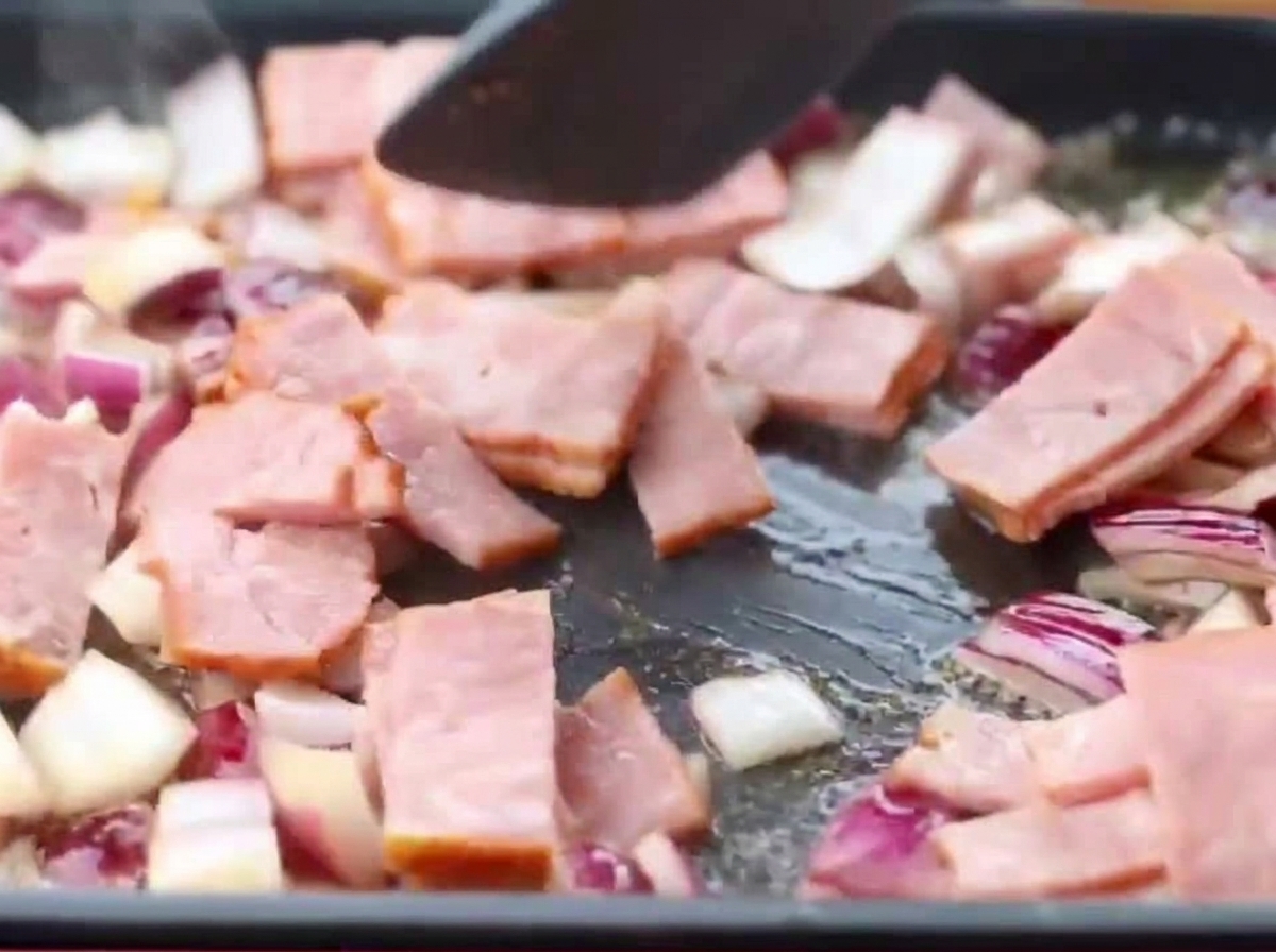 Kawałki boczku i posiekana cebula smażące się razem na patelni.