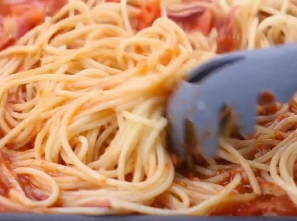 Ugotowane spaghetti dodawane do sosu na patelni.