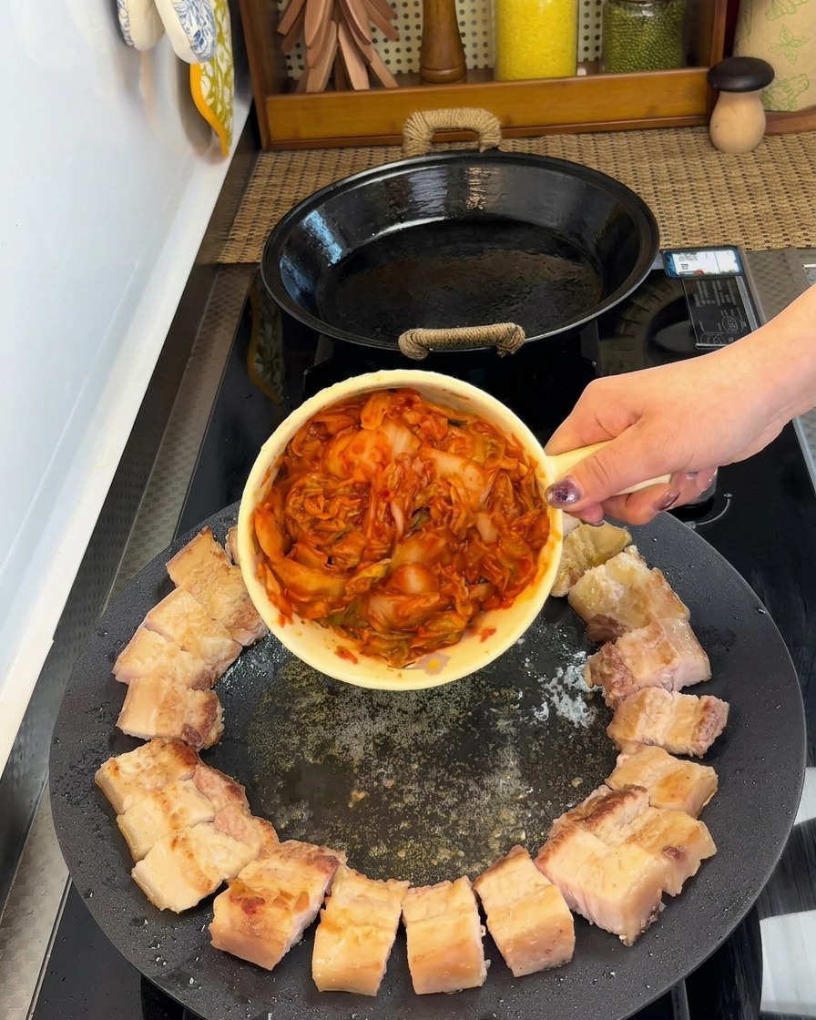 Kawałki boczku ułożone w okrąg na brzegu patelni, w centrum znajduje się porcja kimchi.