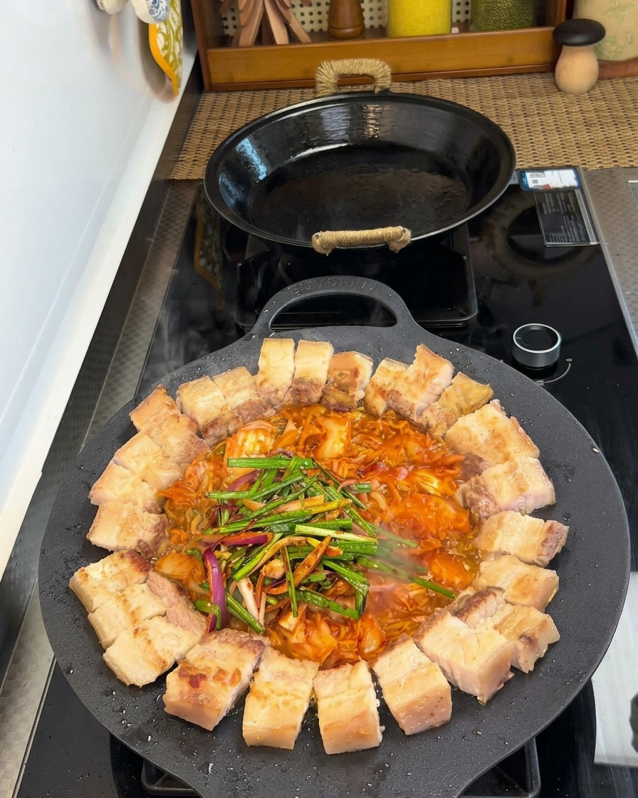 Boczek i kimchi na patelni posypane świeżym porem, cebulą i przyprawami.