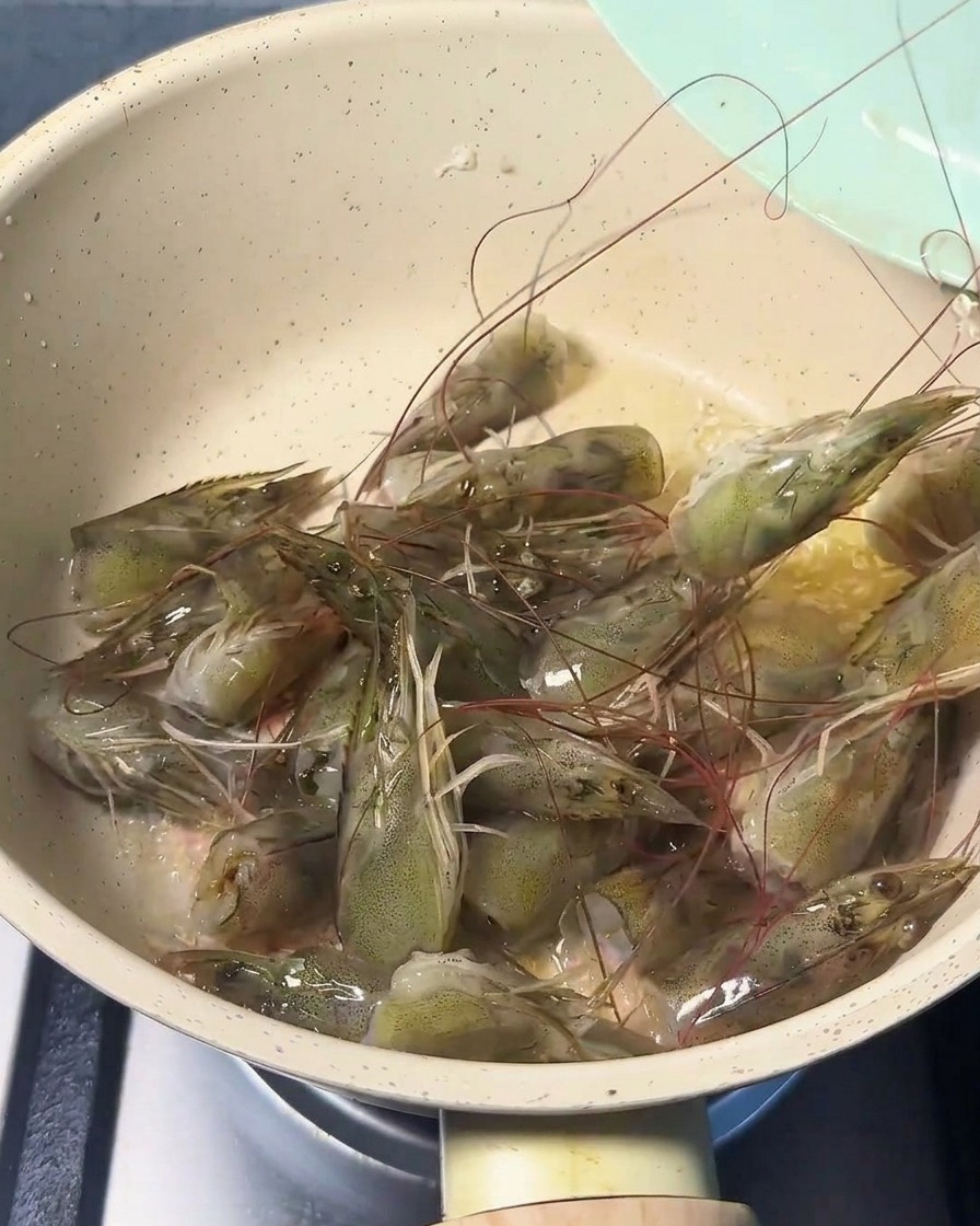 Świeże głowy krewetek smażone na patelni na złocistym oleju, nabierające różowego koloru i uwalniające aromat.