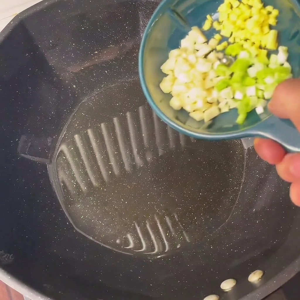 Posiekana zielona cebulka i czosnek smażące się na gorącym oleju w woku.