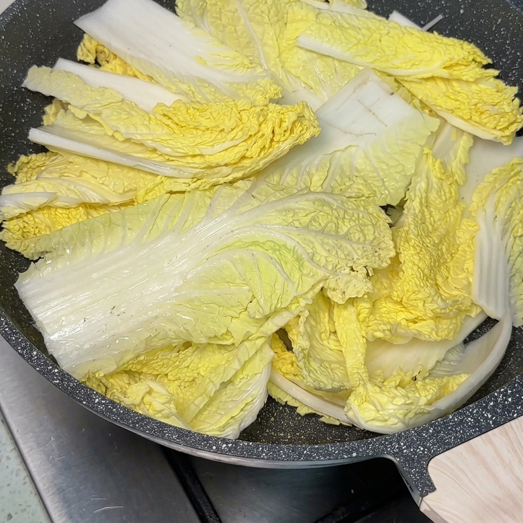 Patelnia wypełniona różnymi składnikami gulaszu z dużą łyżką czerwonej pasty chili na środku, zalewana bulionem.