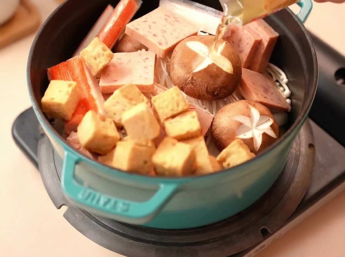 Kawałki tofu rybnego i paluszki krabowe układane w garnku.