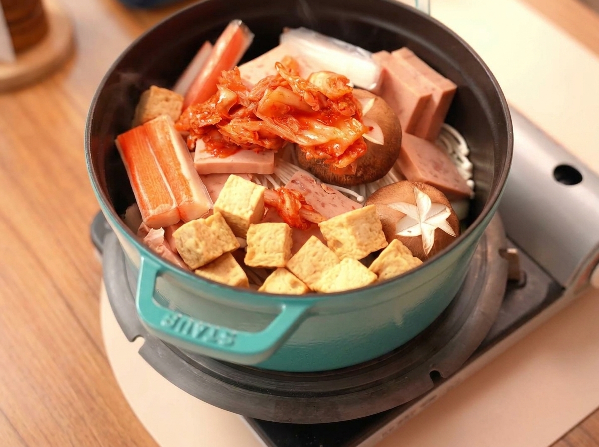 Stos jasnoczerwonego kimchi na środku składników w garnku.