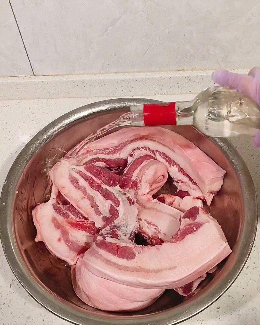 Kawałki surowego boczku w metalowej misce zalewane przejrzystym alkoholem.
