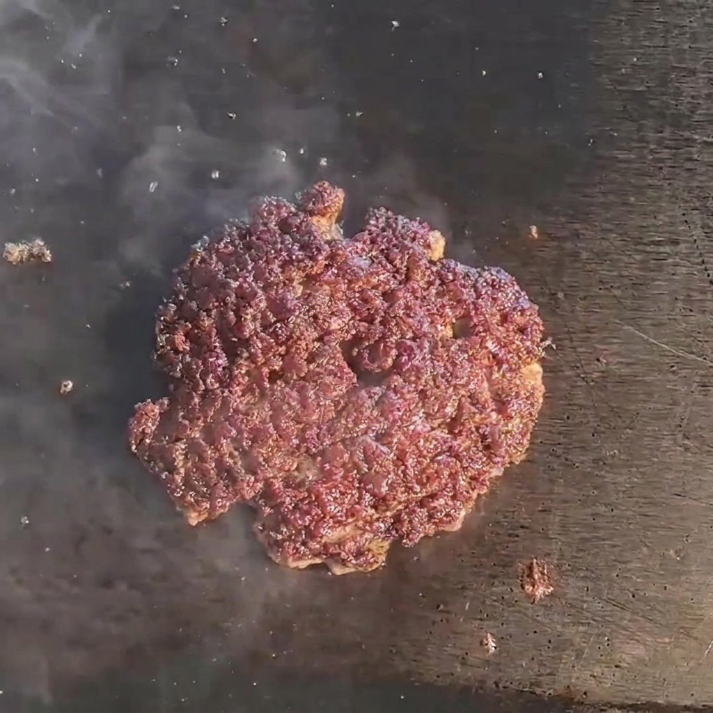 Rozpuszczający się plaster sera na zrumienionym kotlecie wołowym na gorącym grillu.