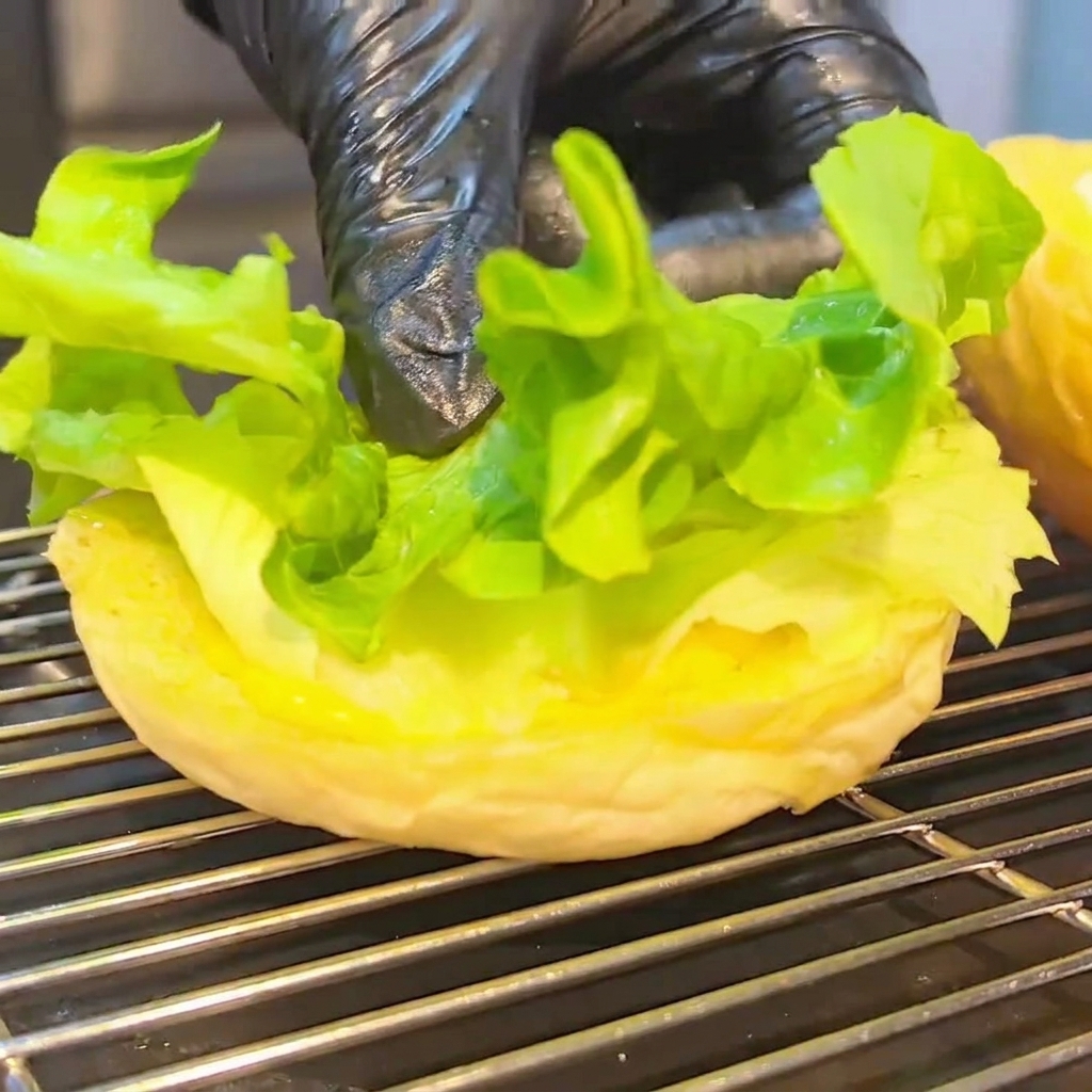 W połowie złożony burger na dolnej bułce, z sałatą, pomidorem, kotletem z serem i bekonem.