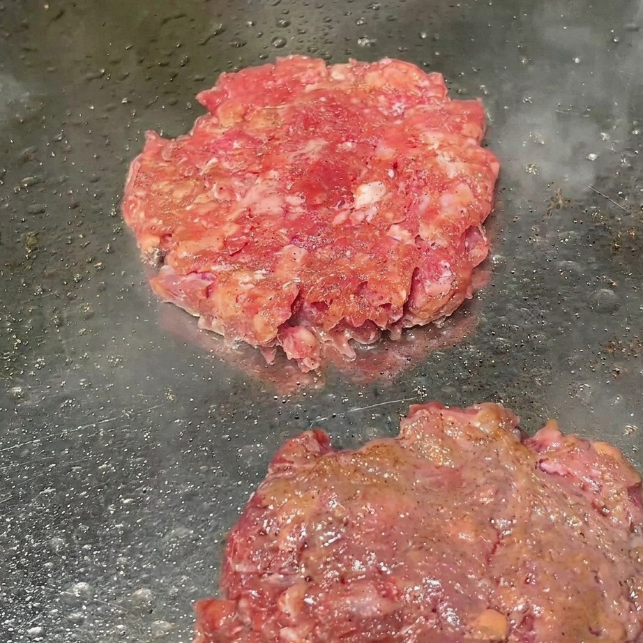 Kotlety wołowe na grillu posypywane świeżo mielonym czarnym pieprzem.