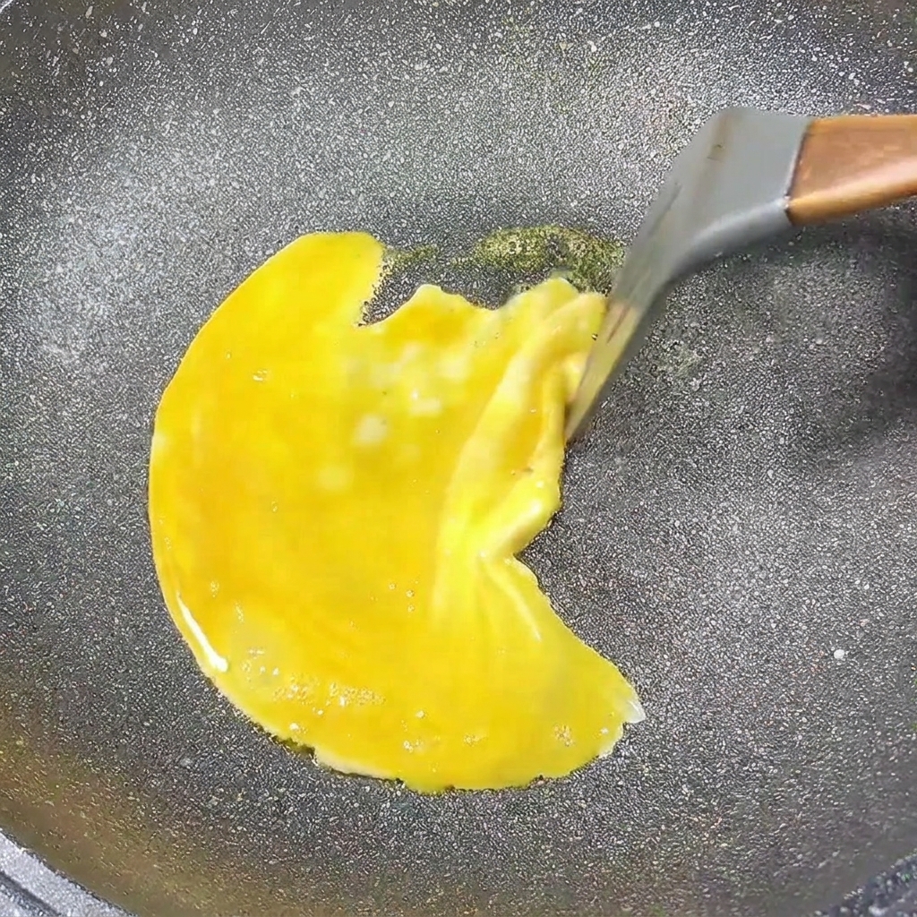 Omlet jajeczny smażący się na patelni, brzegi są delikatnie zsuwane do środka.