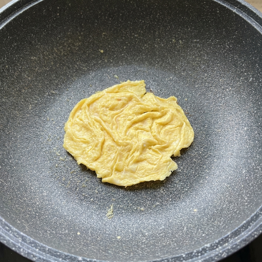 Plaster sera topiący się na wierzchu usmażonego omletu na patelni.