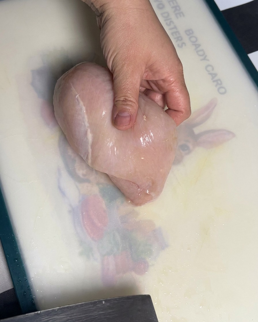 Surowa pierś z kurczaka krojona na równe kawałki na desce do krojenia.