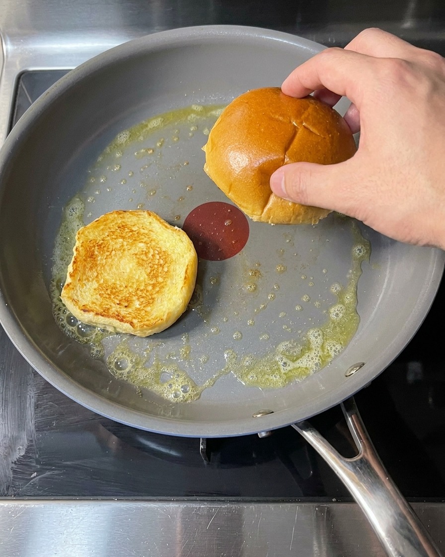 Bułki do burgerów smażące się na patelni z roztopionym masłem.