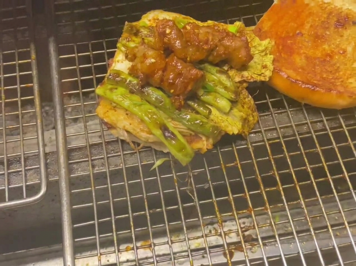 Dolna połówka bułki z grillowanymi warzywami i mięsem na grillu.