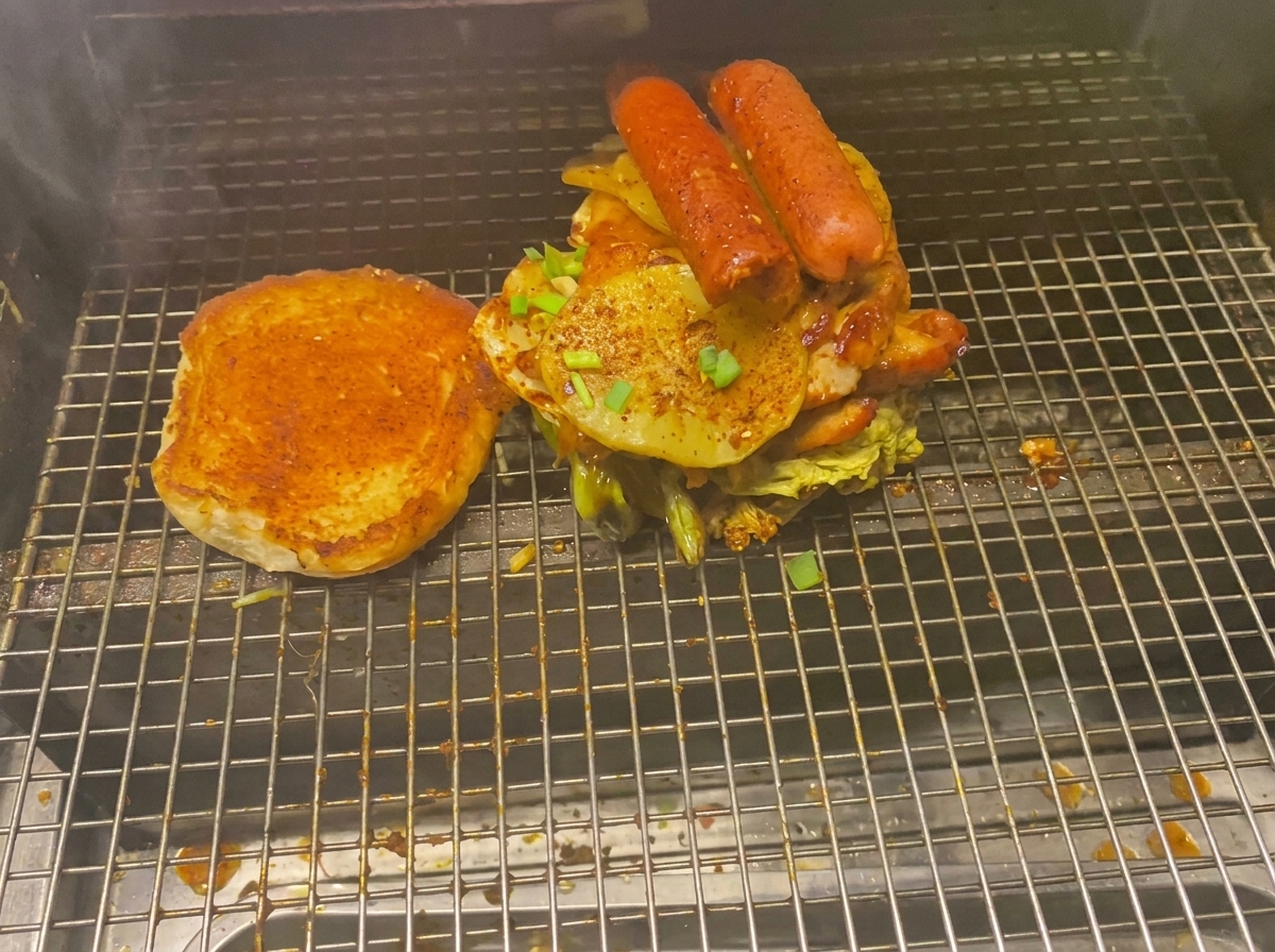 Wieżowy burger z mięsem, ziemniakami i kiełbasą obok bułki na ruszcie.