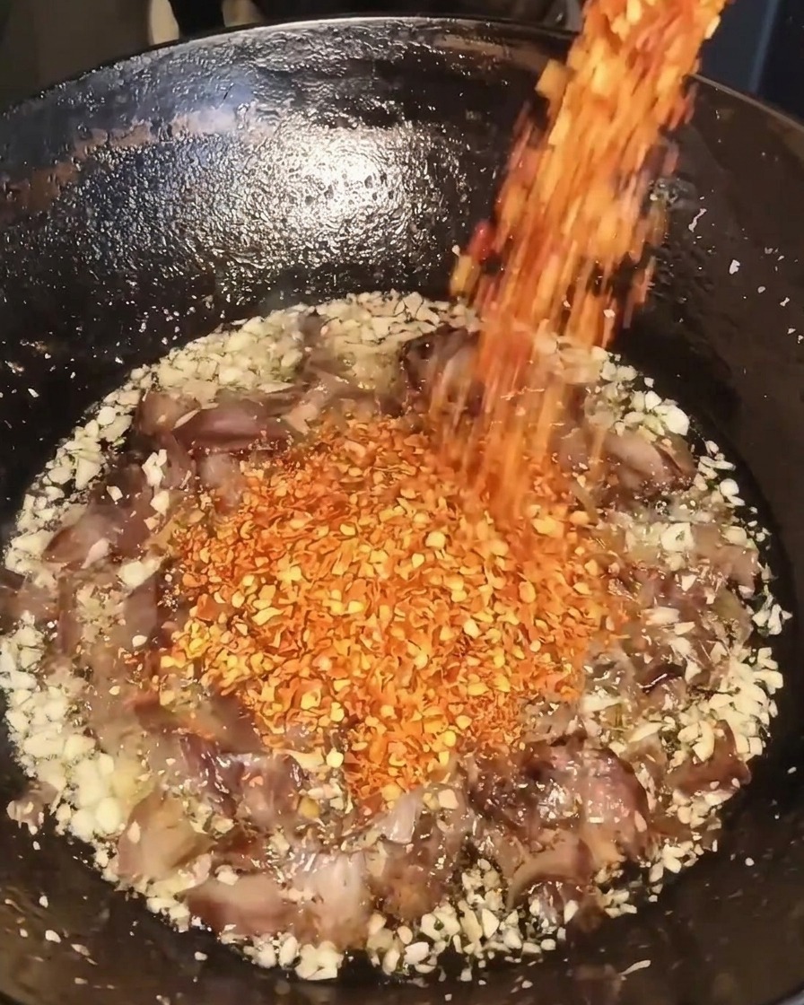 Suche płatki czerwonego chili wsypywane do woka z wołowiną, czosnkiem i olejem.