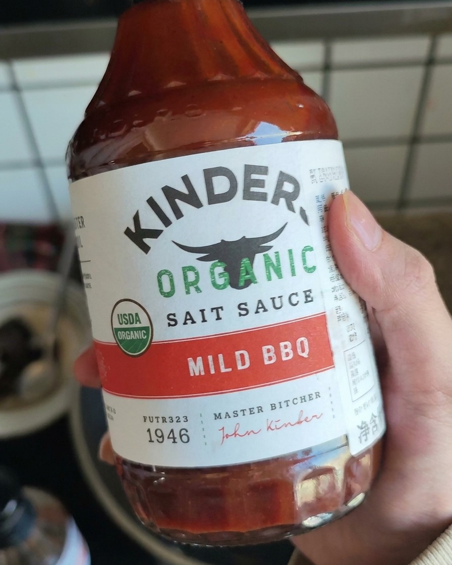 Ręka trzymająca butelkę łagodnego sosu BBQ, przygotowująca się do dodania go do szarpanej wieprzowiny.