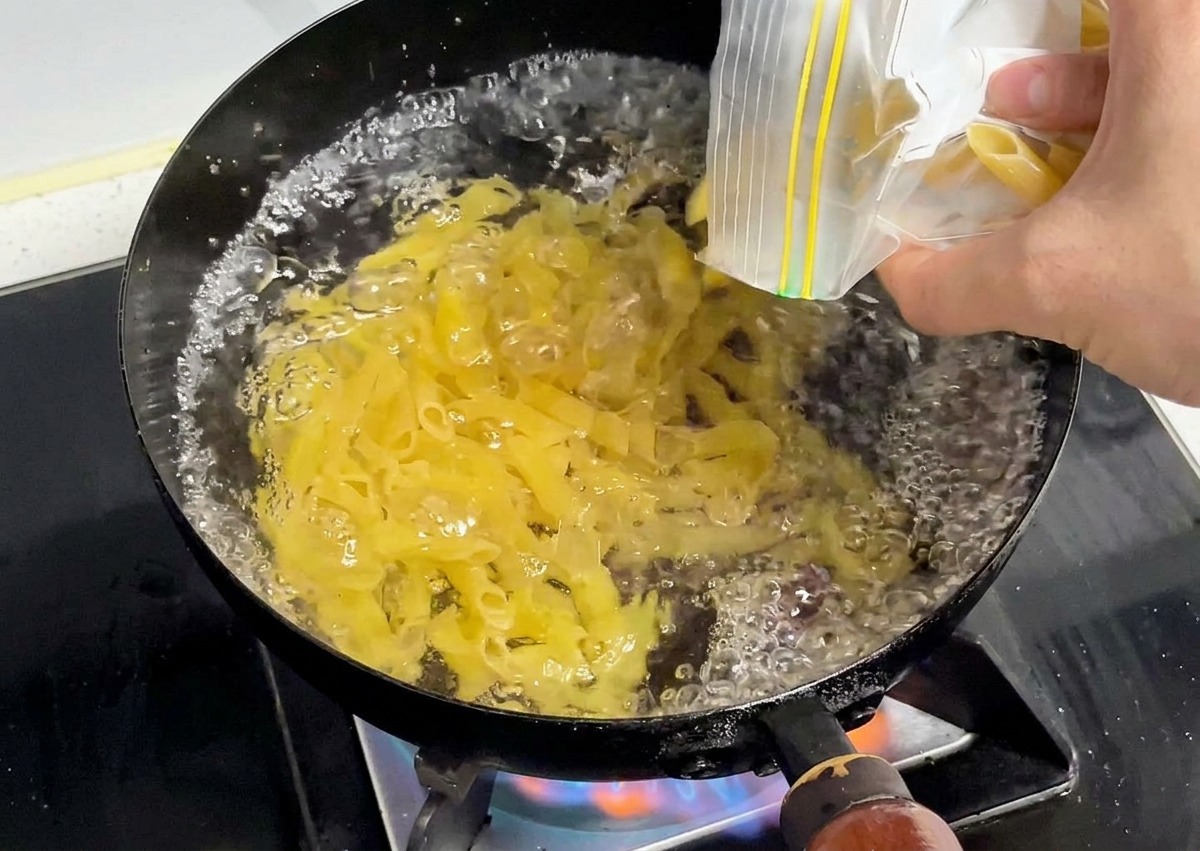 Surowy żółty makaron penne wsypywany do garnka z intensywnie wrzącą wodą.