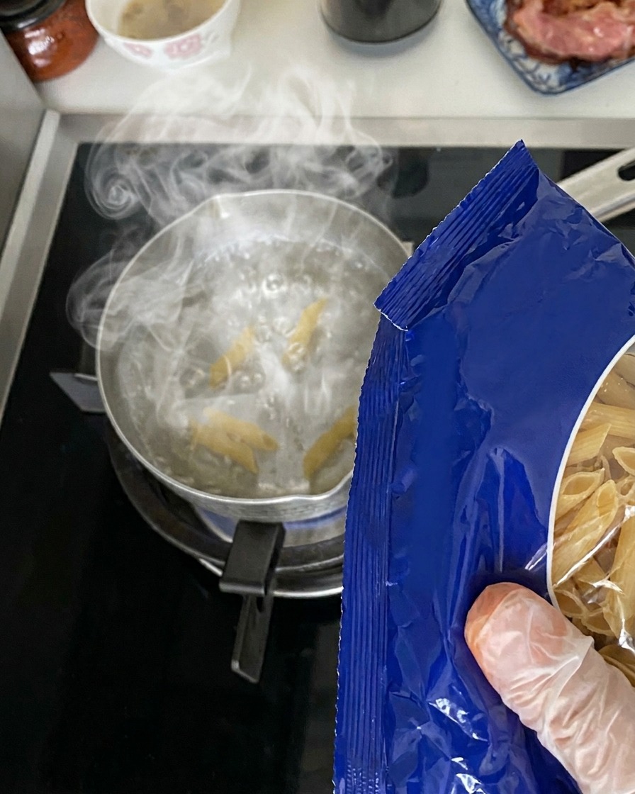 Makaron penne wsypywany do garnka z wrzącą wodą.