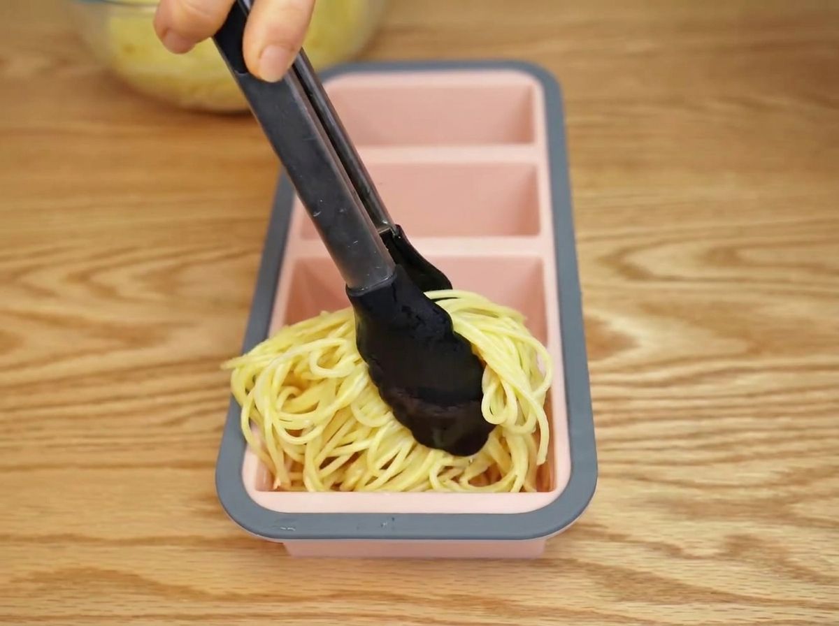 Ugotowane spaghetti przekładane do silikonowej formy za pomocą szczypiec.