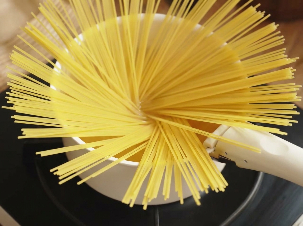 Porcja suchego spaghetti wrzucana do garnka z wrzącą, osoloną wodą.