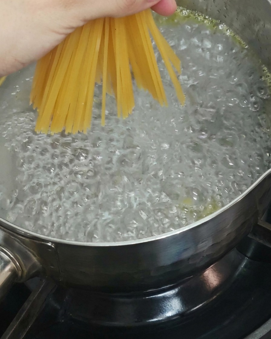 Dłoń trzymająca pęczek suchego spaghetti wkładanego do gotującej się wody.